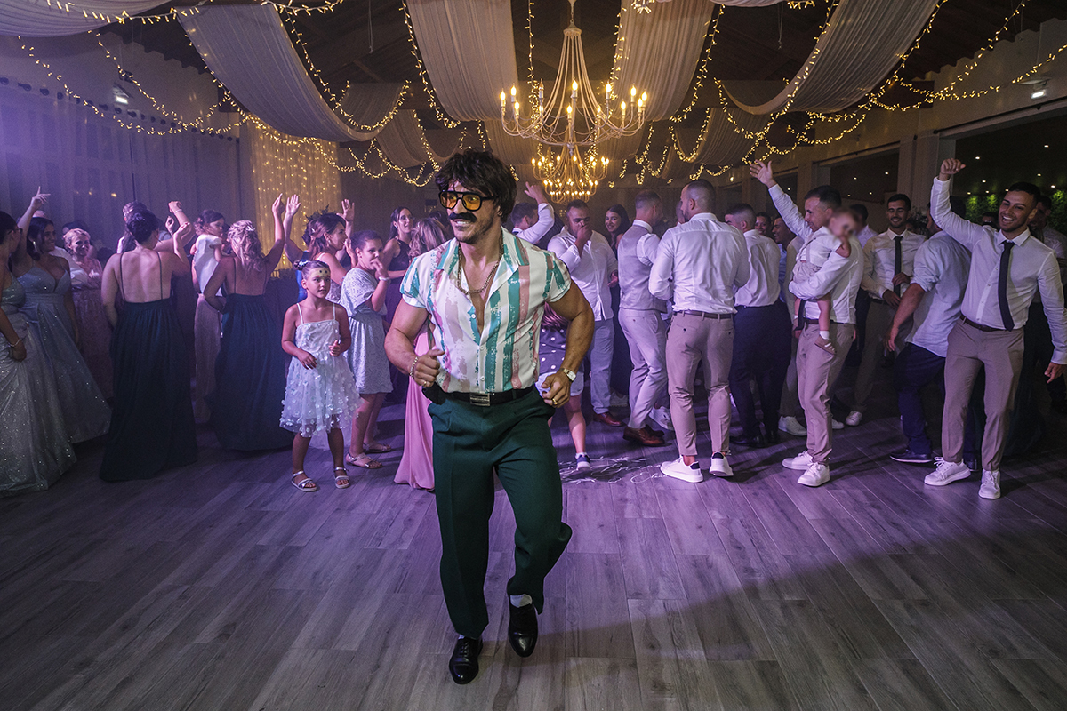 Aqui vemos novamente o Sr. Camaleão no centro da pista a dançar, com os convidados atrás também a dançar e a acompanhar a energia da festa.