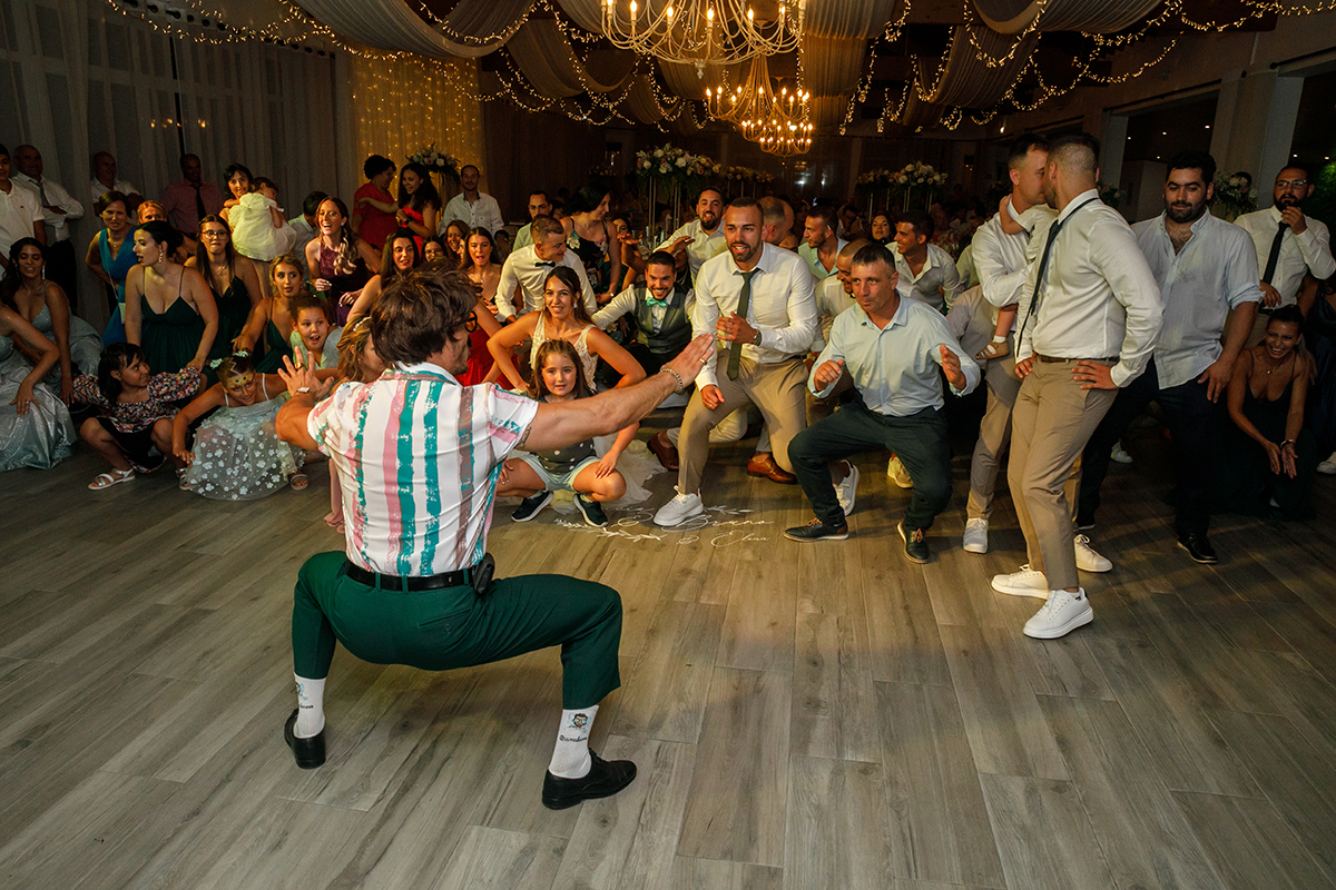 O Sr. Camaleão aparece agachado e com os braços no ar, de costas para a câmara, enquanto os convidados à frente o imitam cheios de alegria.