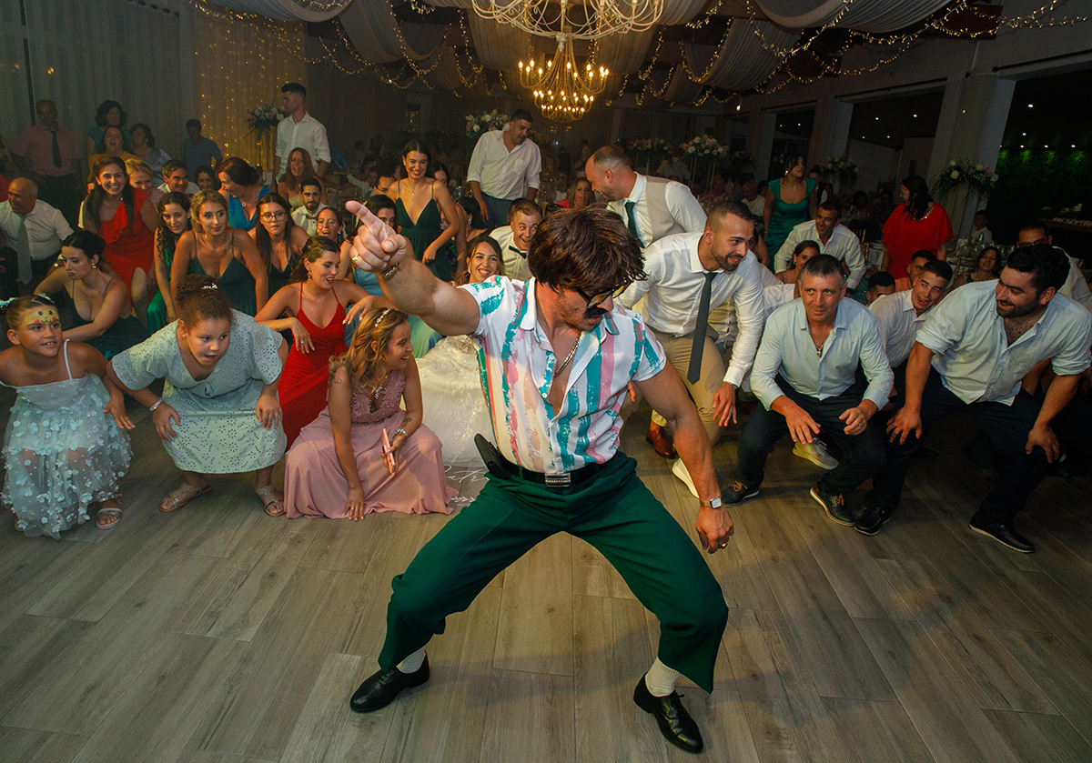Nesta, o Sr. Camaleão está de frente para a câmara, ligeiramente de lado, agachado com um braço no ar e um dedo apontado para cima. Atrás, os convidados acompanham a coreografia com entusiasmo.