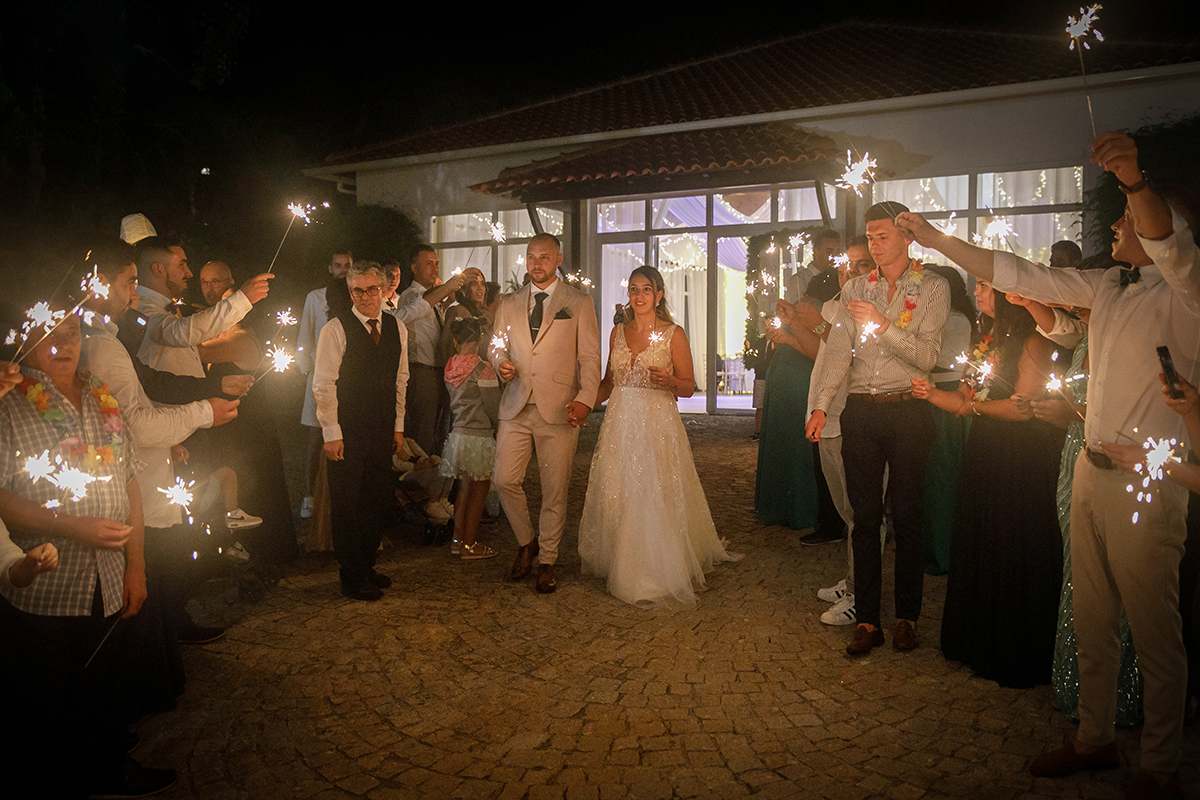 Lá fora, os noivos caminham lado a lado com sparkles nas mãos, rodeados pelos convidados também com sparkles. Um momento mágico e bonito, cheio de simbolismo.