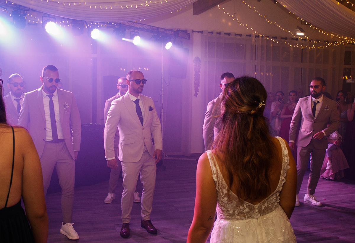 De frente vemos o noivo e os amigos, e de costas a noiva e as amigas. Todos se olham entre si, num momento captado sob uma luz rosa que dá um toque especial à cena.