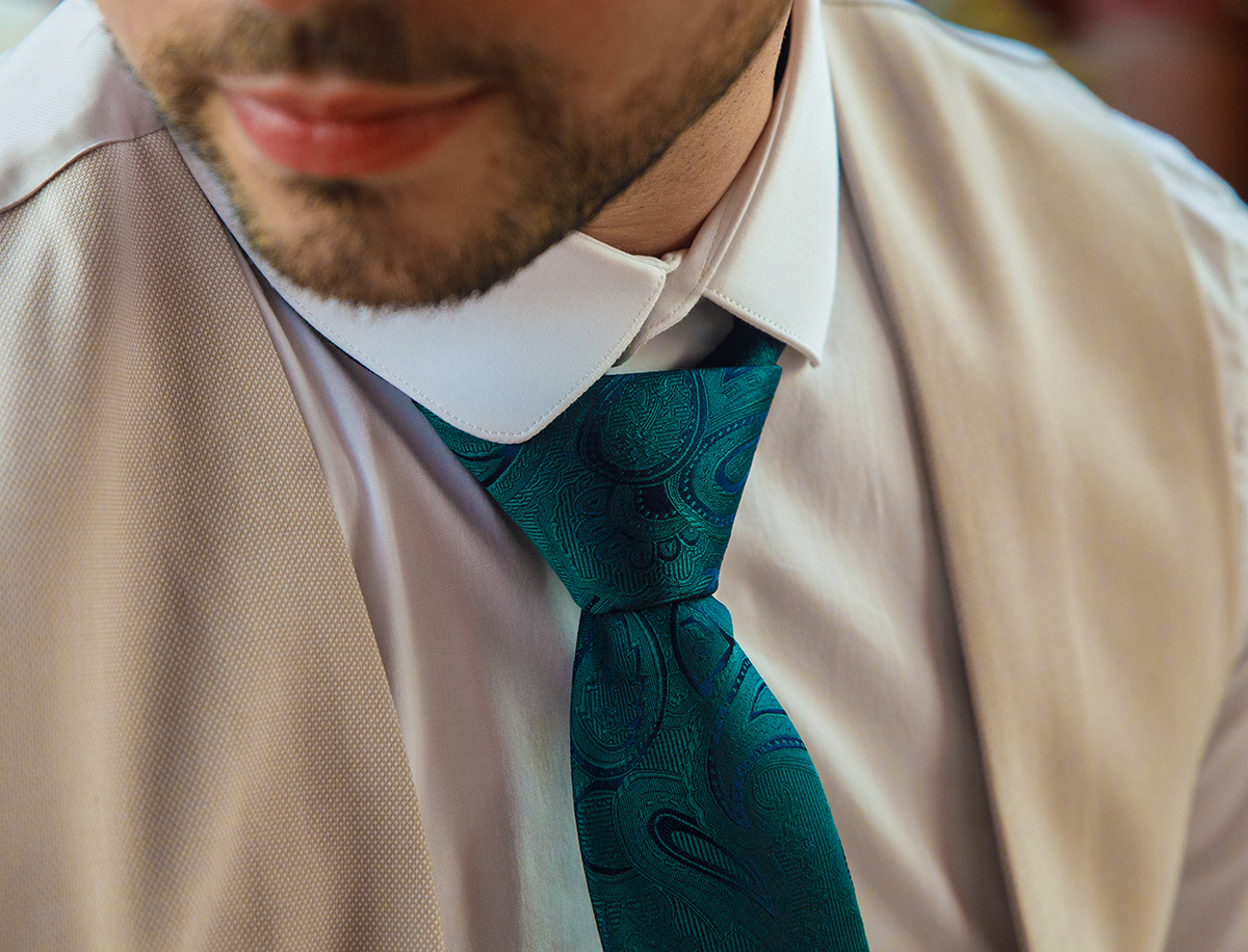 Um plano de detalhe revela a elegância do noivo: colete bege, camisa branca e uma gravata verde que evoca esperança.