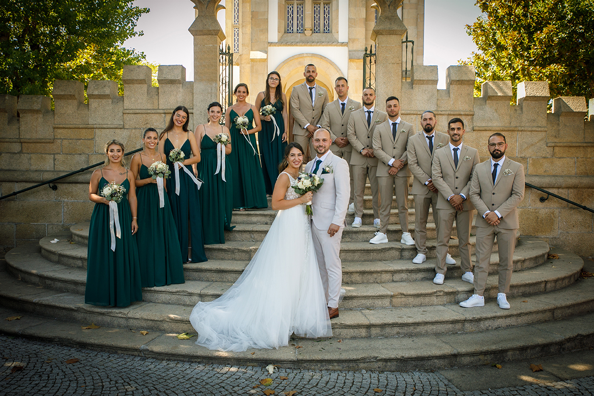 Uma composição perfeita: os noivos no centro, rodeados pelas madrinhas de verde e pelos padrinhos de bege, todos a sorrir para a câmara como uma família de corações entrelaçados.