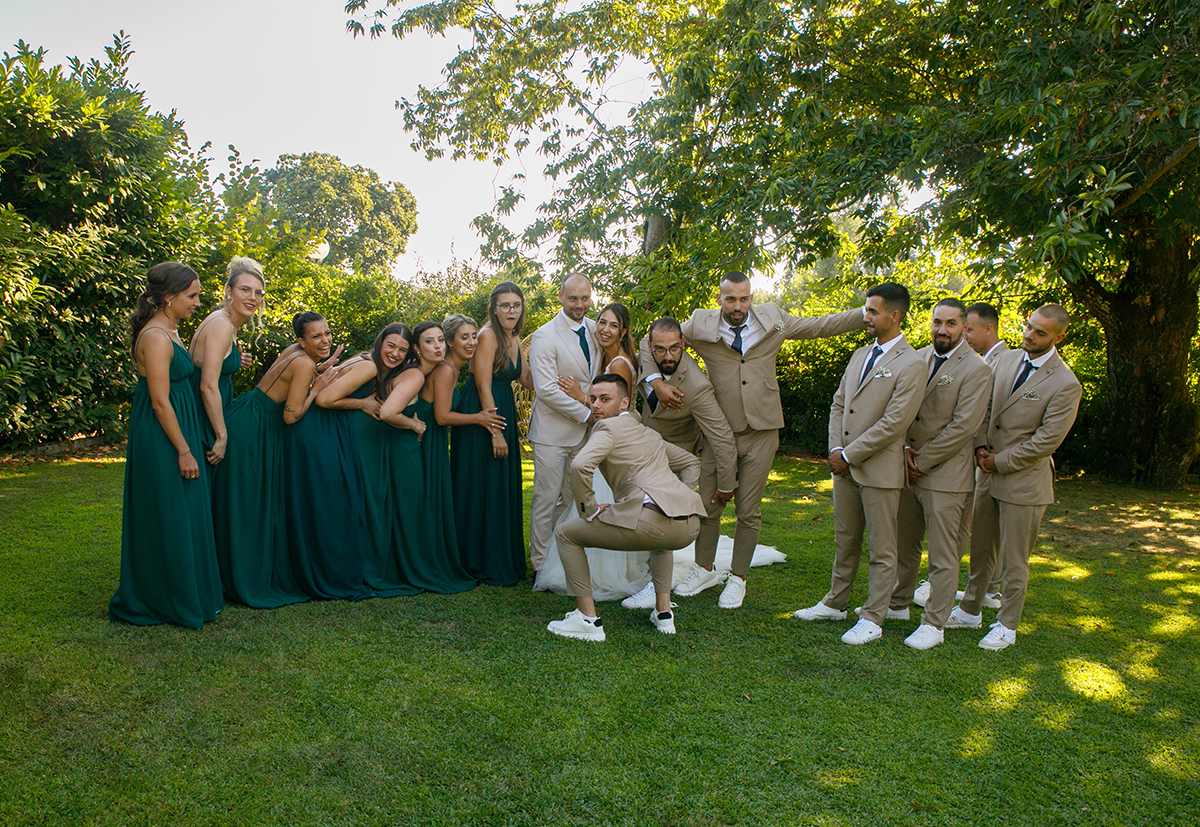 Em grupo, amigos e amigas formam uma moldura em torno dos noivos, enquanto um dos amigos diverte todos com uma brincadeira espontânea.