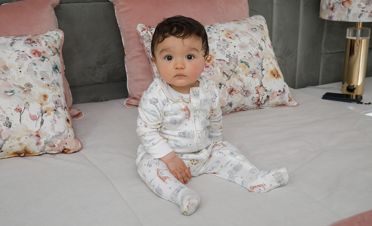 Sentado sobre a colcha branca da cama, Francisco observa a câmara com seriedade. Atrás dele, almofadas floridas e rosadas envolvem o cenário num abraço suave, enquanto o seu corpo, meio reclinado, parece repousar num instante de descoberta silenciosa.