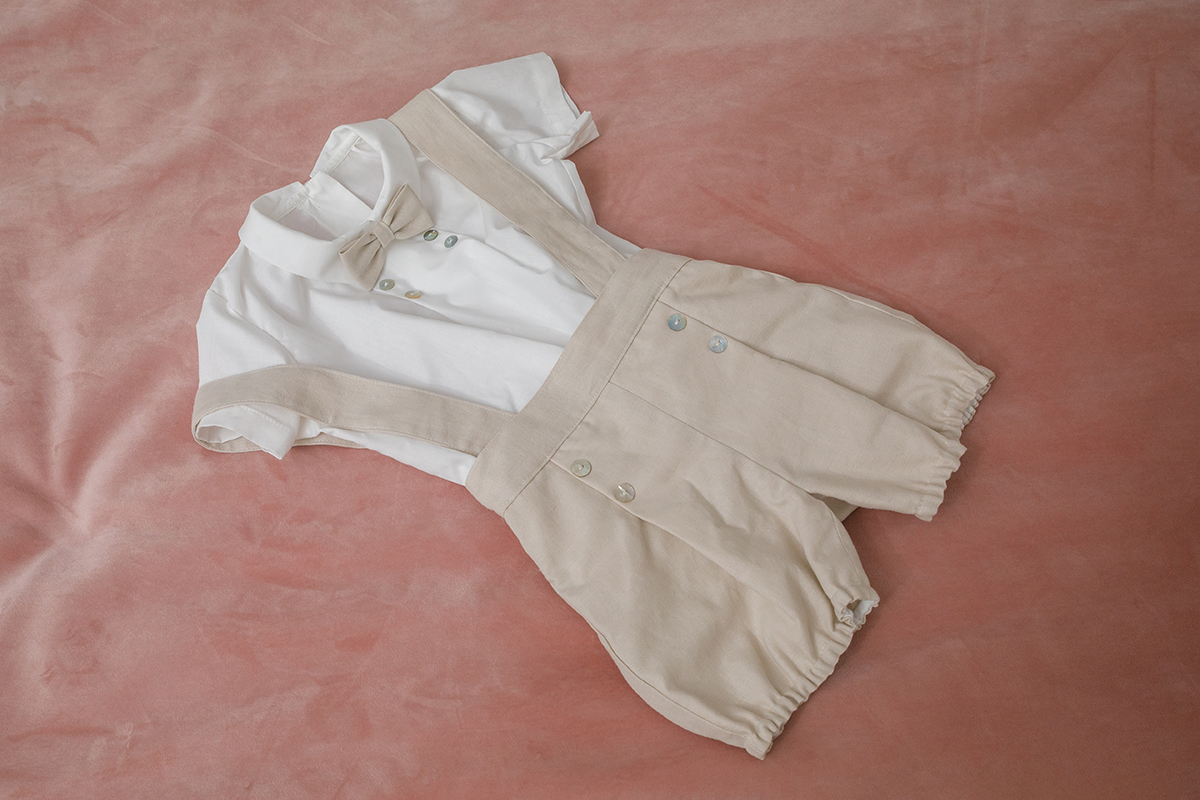 O fatinho repousa sobre a colcha rosa, em tons de branco e bege. A delicadeza do tecido e o cuidado na disposição transmitem o carinho com que cada detalhe foi pensado. Um símbolo de pureza e celebração.