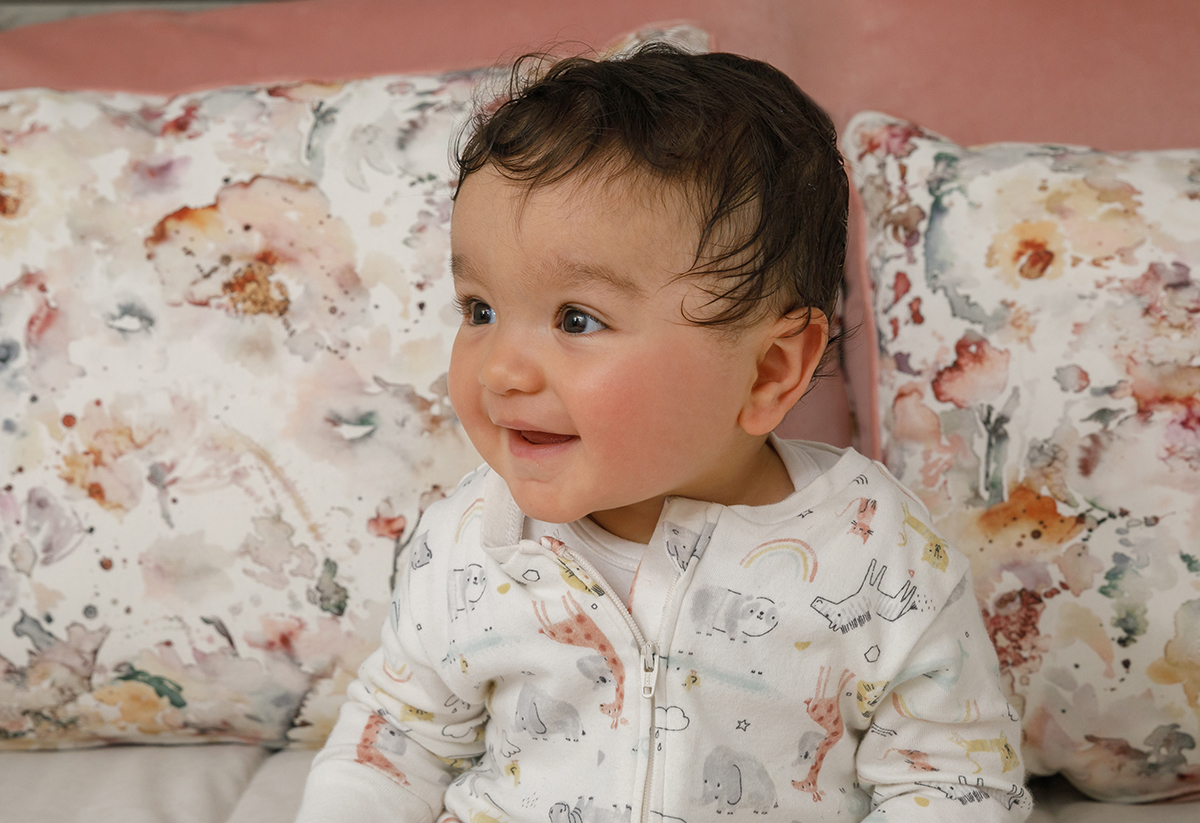 Com um sorriso rasgado e olhar desviado para o lado, Francisco surge da cintura para cima, irradiando felicidade. Atrás dele, as almofadas floridas e rosa compõem um retrato leve e doce da infância em festa.