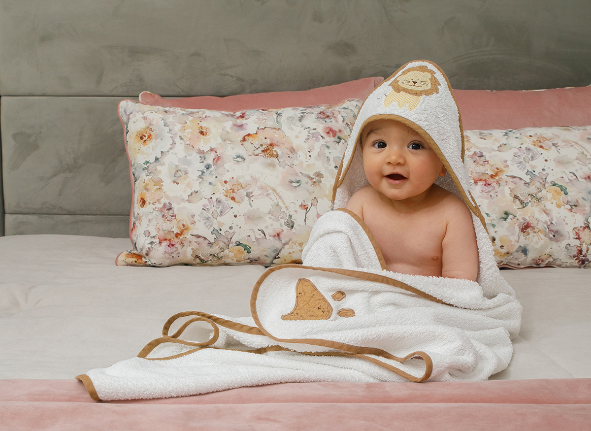 Sentado no lado direito da imagem, Francisco sorri para a câmara, envolto no seu robe/toalha que se estende até ao lado oposto da foto. Um abraço de tecido que aconchega a ternura deste instante.