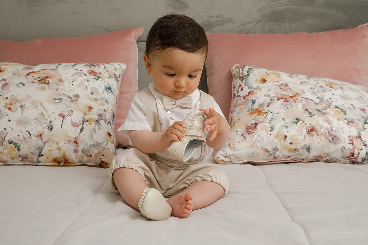 Francisco observa o próprio sapato, com um pé calçado e o outro não. Sentado sobre a colcha branca, o seu olhar atento e concentrado revela a beleza dos pequenos gestos.