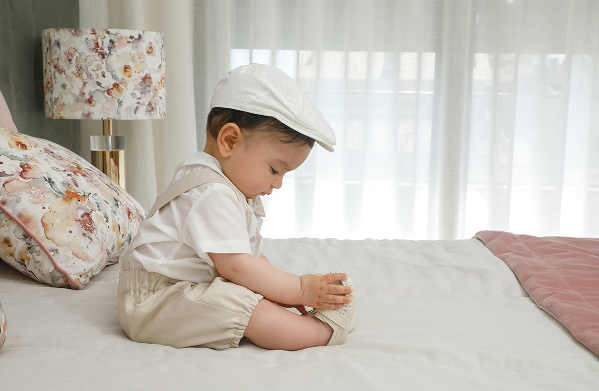 Num plano lateral, Francisco observa os próprios pés com entusiasmo. A almofada florida atrás repete-se como cenário familiar e confortável.