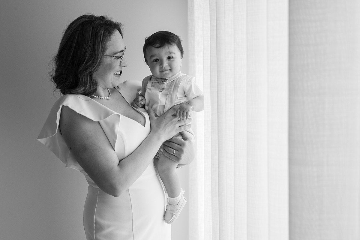 A mãe segura-o ao colo, ambos sorridentes, junto à janela. Num plano da cintura para cima, o carinho no olhar partilhado entre os dois é um retrato de amor eterno.