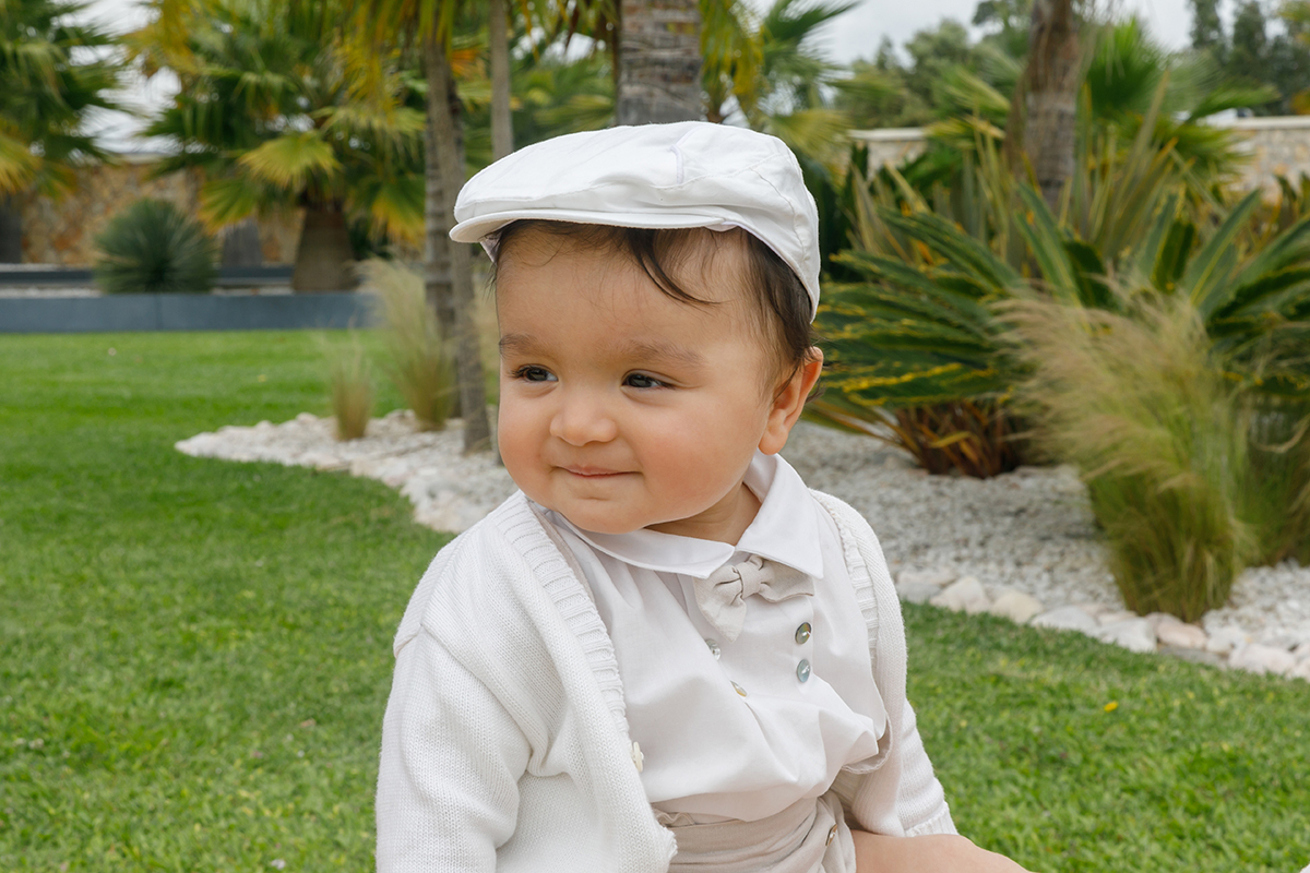 Do lado de fora, Francisco é visto da cintura para cima, sorridente e ligeiramente de lado. O jardim ao fundo, com relva e palmeiras, emoldura a sua presença alegre.