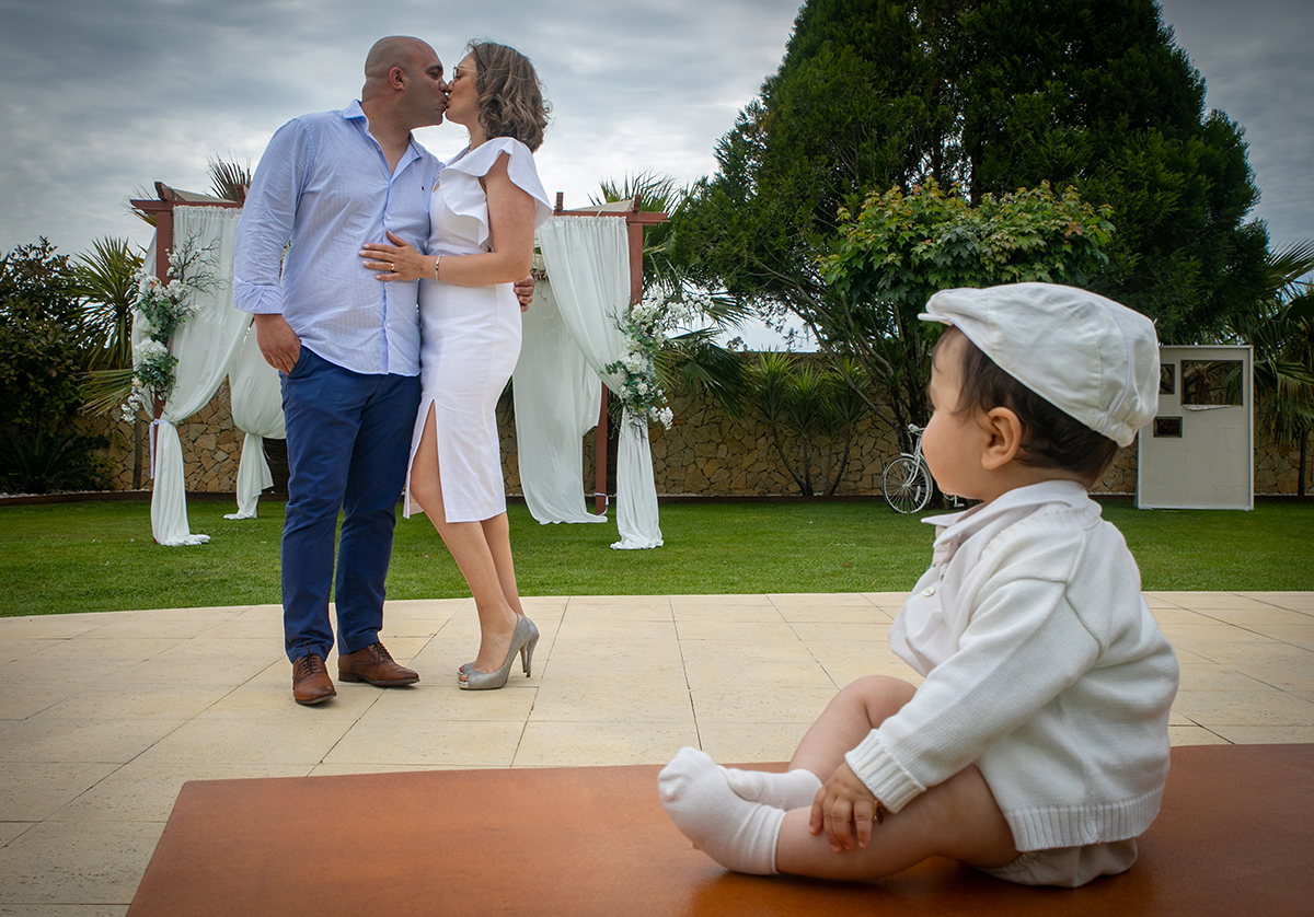 À esquerda, os pais beijam-se, unidos num gesto íntimo. À direita, Francisco, agora com o casaquinho e a boina, observa-os com ternura. O amor que os une revela-se em cada gesto.