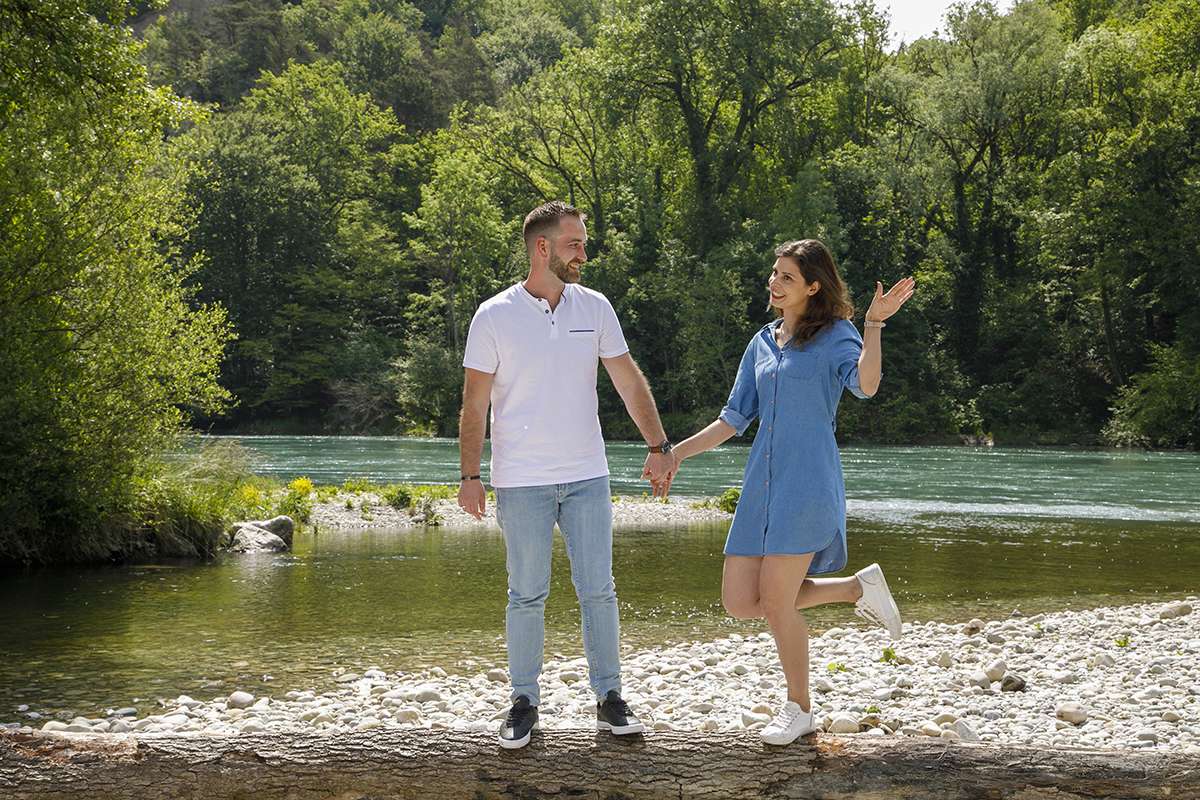 Ainda no caminho de pedras, os dois estão lado a lado, sorridentes. Olham um para o outro com cumplicidade, e Marta levanta uma das mãos e uma perna, num gesto espontâneo e divertido. Ao fundo, o rio e a natureza compõem um cenário cheio de vida.