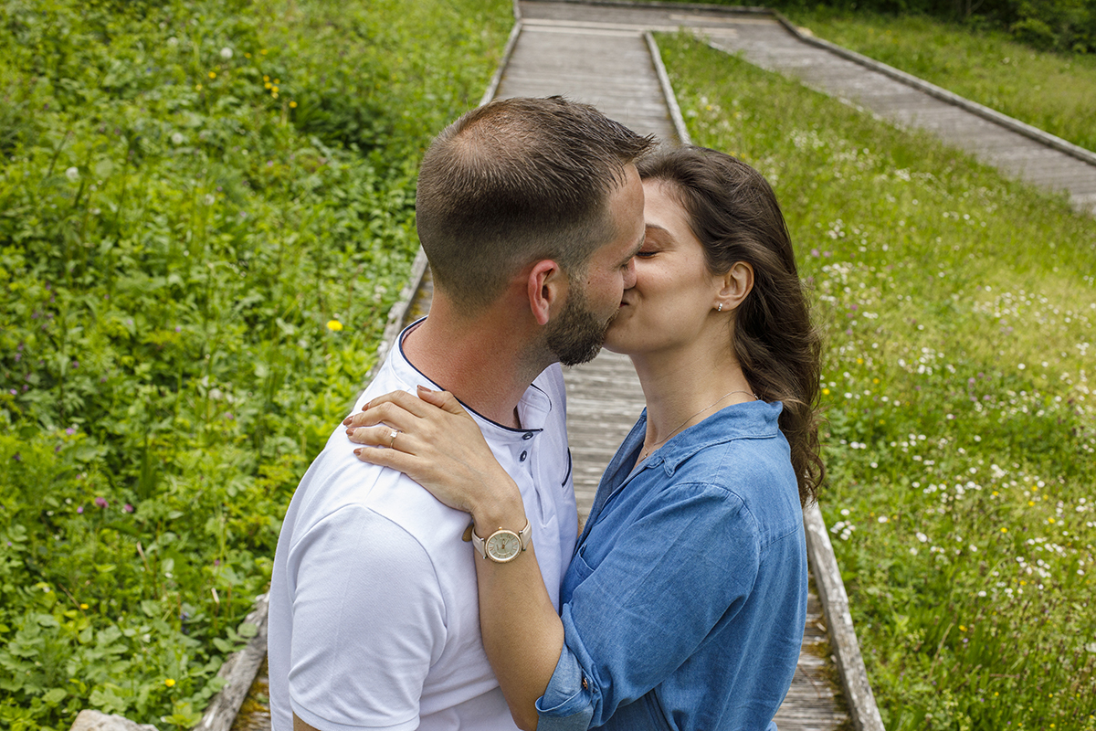 De um ângulo picado, vemos o casal a beijar-se no centro da imagem, sobre passadiços de madeira rodeados por erva. Marta apoia a mão no ombro de Mathieu. Um beijo terno numa envolvência natural.