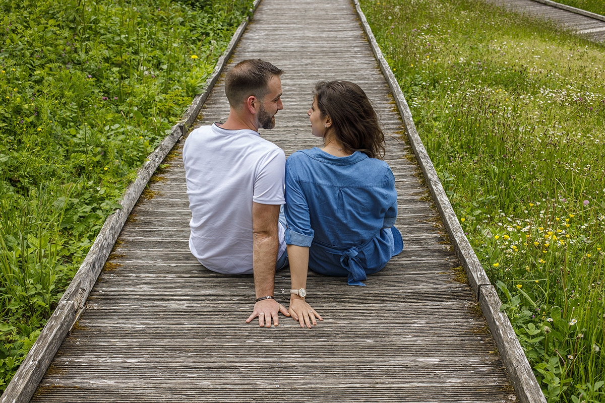 Ainda nos passadiços, os dois estão sentados, com uma mão apoiada atrás. Olham-se com amor e carinho, partilhando um momento sereno e cúmplice.