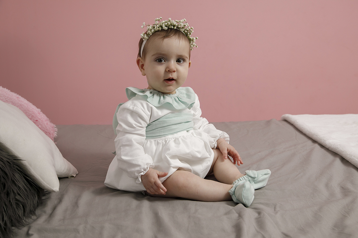 De novo sobre a cama, com as mãozinhas nos joelhos, Valentina fita a câmara com seriedade. O silêncio do instante fala mais alto que as palavras.