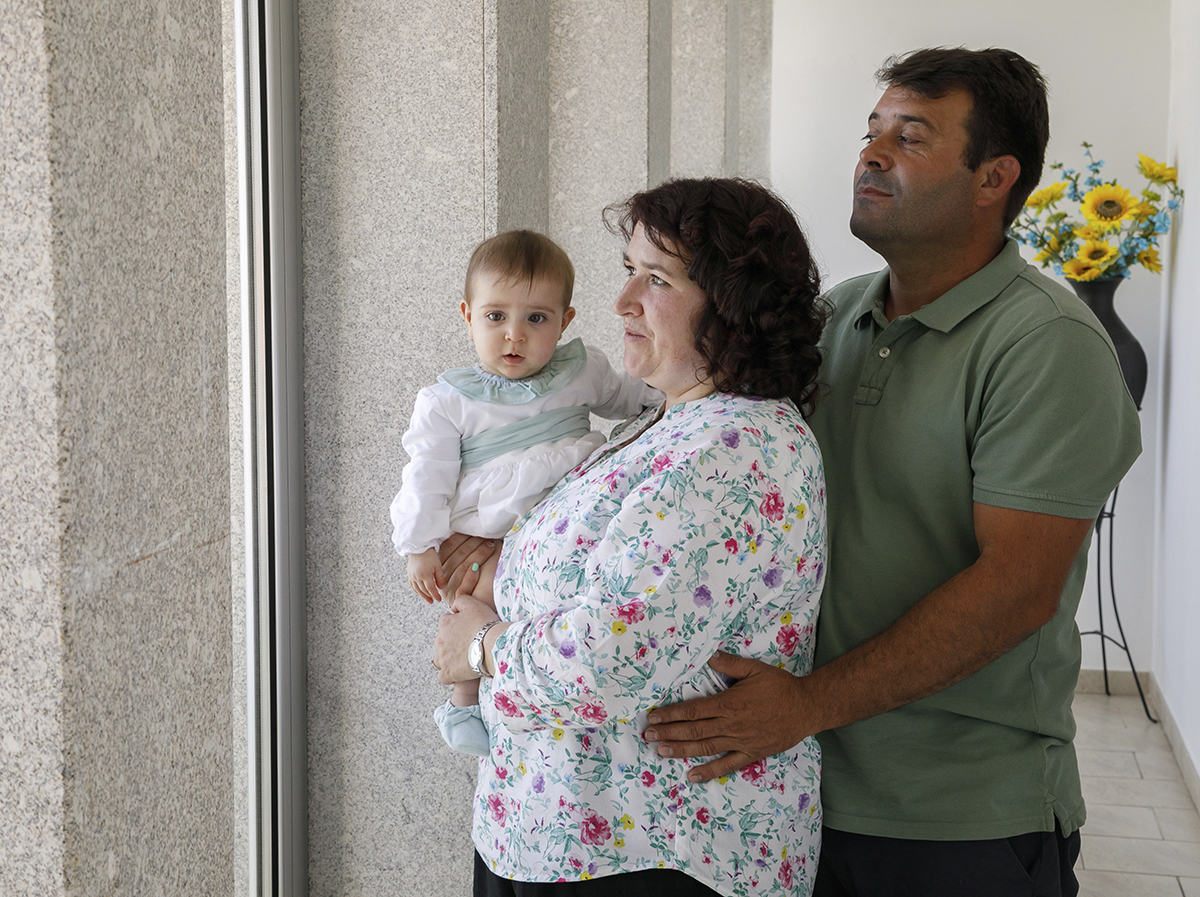 Mãe e filha estão abraçadas, com o pai atrás, a envolvê-las. Todos olham para a janela com seriedade. Valentina, com o olhar fixo na câmara, transmite paz e força.