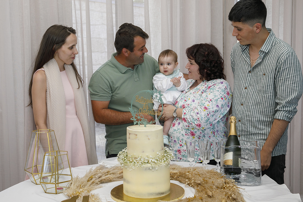 Num plano mais afastado, os padrinhos e os pais alinham-se dos lados, com Valentina no centro. Todos sorriem para ela, enquanto ela mantém um olhar sério e atento. Uma estrela no centro de um círculo de amor.