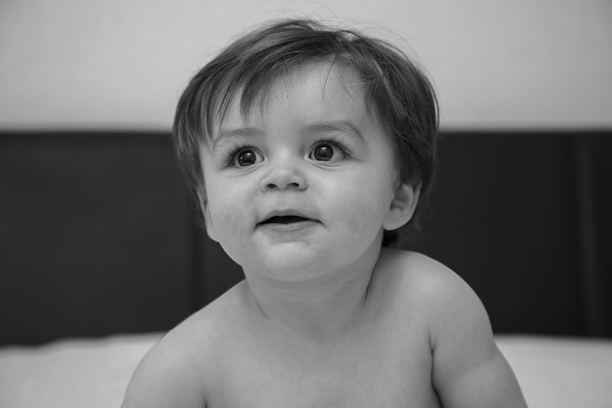 A preto e branco, um retrato íntimo do Gabriel, do peito para cima. No centro da imagem, olha para cima e para o lado com um sorriso leve e expressão serena, um instante de pureza captado no tempo.