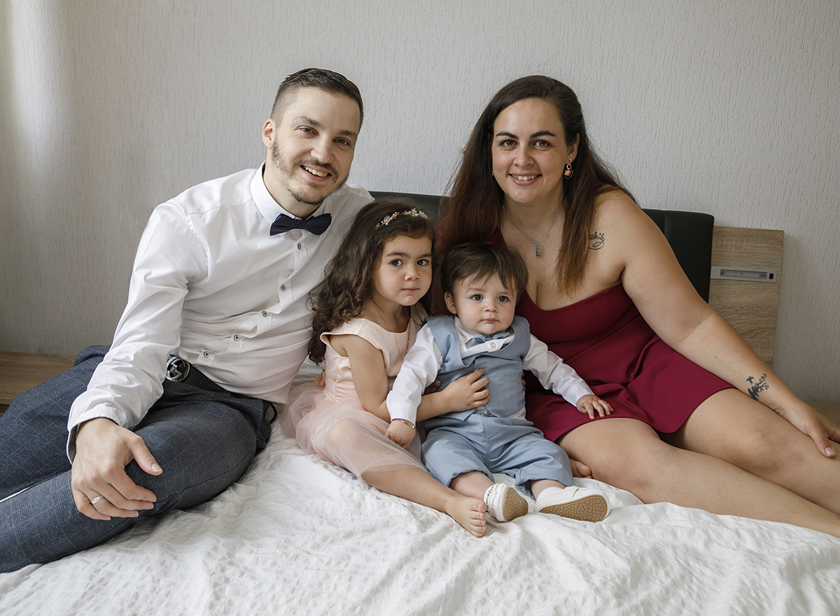 Num plano mais afastado, a família completa-se na imagem. Pai e mãe nos extremos, os filhos ao centro. Todos olham para a câmara com sorrisos genuínos, num retrato de união e felicidade.