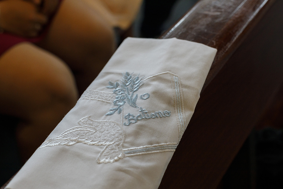 Pendurado no banco da igreja, o pano de Batismo do Gabriel revela os seus detalhes azul e branco. O bordado fino e o tecido leve testemunham a solenidade do momento.