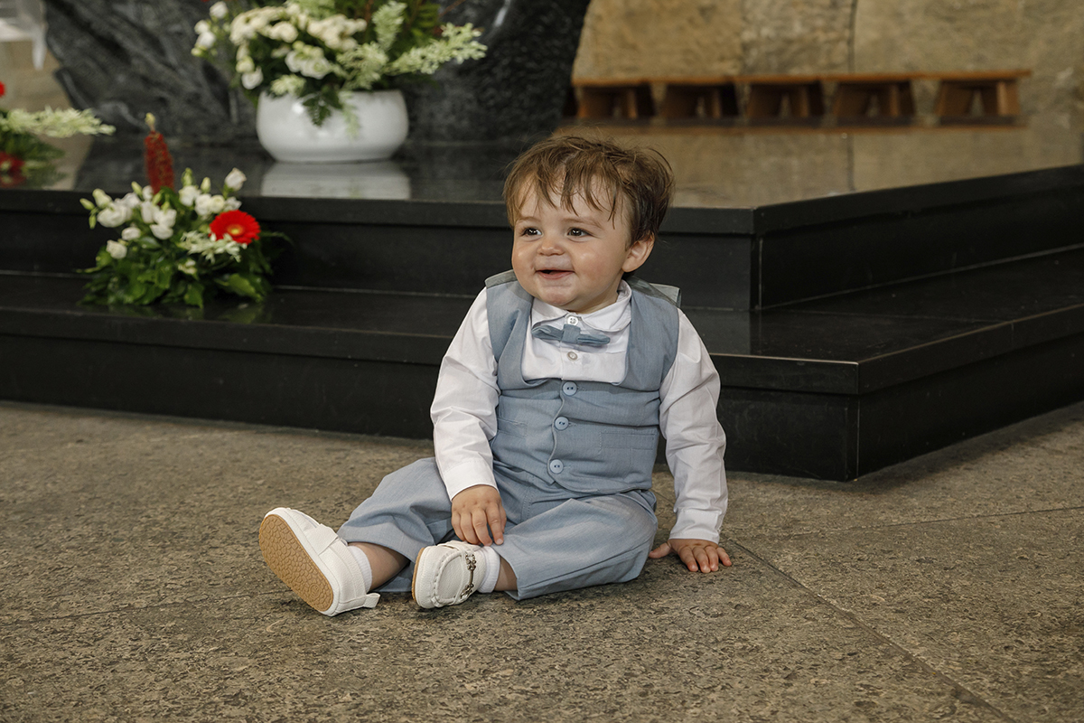 Agora de corpo inteiro, no chão, ele apoia-se com uma mão e mantém a outra entre as pernas. Olha para o lado com um sorriso confiante, um pequeno explorador no seu grande dia.