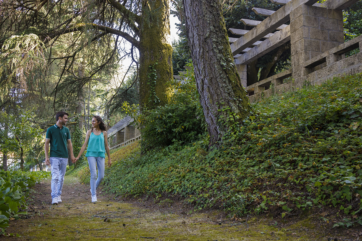 Diana e André descem de mãos dadas por uma rampa envolta em verde, trocando olhares cúmplices e sorrisos apaixonados.