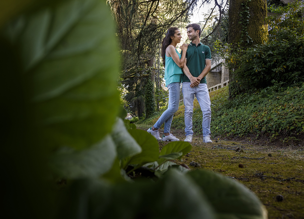Folhas verdes emolduram o lado direito da imagem, enquanto Diana e André, no lado oposto, se mantêm serenos, ligados pelo olhar e pelo gesto.