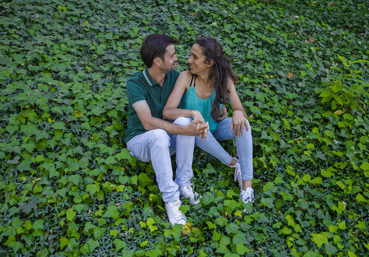 Sentados entre trepadeiras, lado a lado, Diana e André trocam um olhar sereno enquanto dão as mãos, um momento de sintonia perfeita.