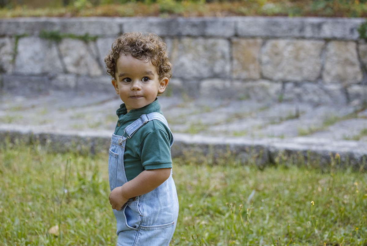 Tomé surge de perfil, sobre a relva, com o olhar curioso e o fundo suavemente desfocado. A infância capturada num instante mágico.