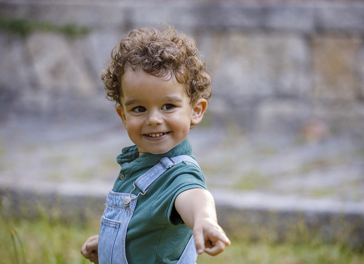 Em plano aproximado, Tomé aponta e sorri com alegria genuína, o fundo desfocado realça ainda mais a sua expressão encantadora.