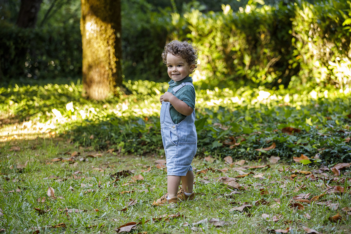 Num cenário verde e aberto, Tomé caminha com confiança, mãos nas alças do macacão, sorriso no rosto e um ar traquina de quem está pronto para novas aventuras.