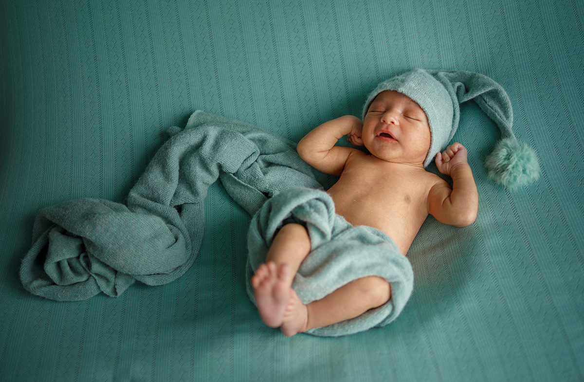 Sobre um fundo verde harmonioso, Daniel dorme do lado direito da imagem. O verde da roupa combina com a manta que o envolve suavemente, enquanto o seu gorro com pompom dá o toque final de fofura a esta composição poética.