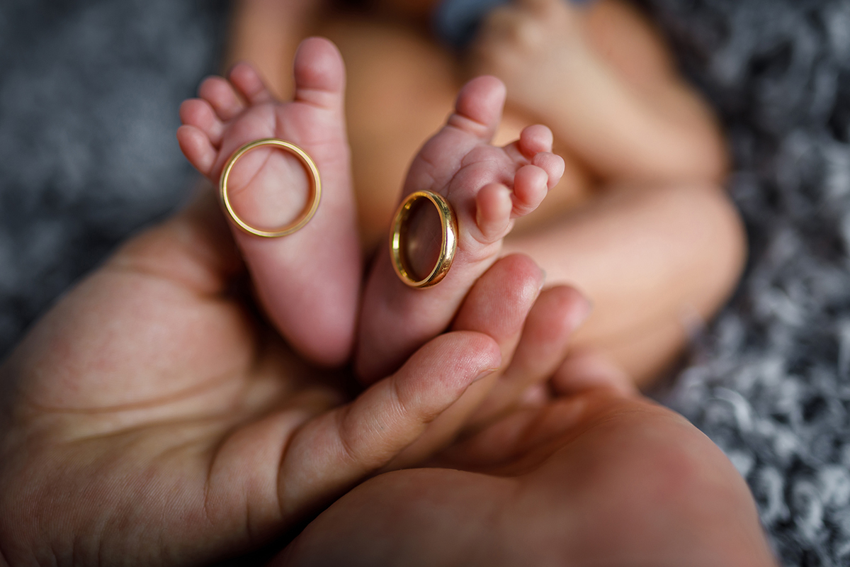  Um plano com vinheta revela os pezinhos de Daniel entre mãos protetoras. Em cada pé, uma aliança: símbolo de amor eterno. O fundo desfocado acentua a preciosidade deste detalhe mágico.