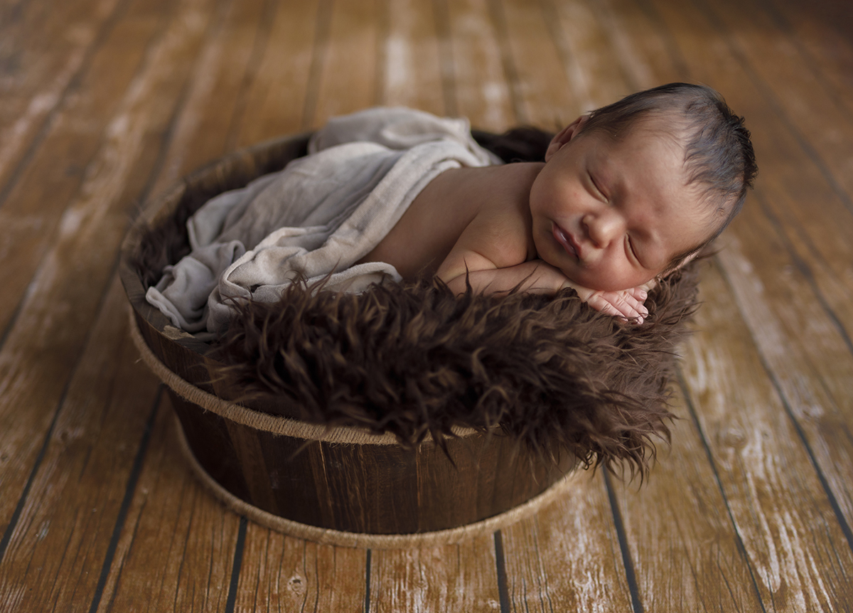Envolvido numa cestinha de madeira forrada com uma manta castanha fofa, Daniel dorme de barriga para baixo com as mãos sob a carinha. Tapado até à cintura com um lençol branco, parece estar aninhado num ninho de amor.