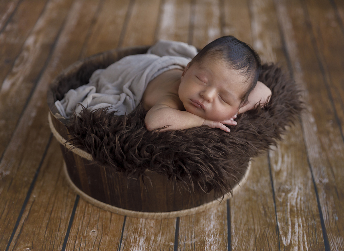 Ainda na cestinha, Daniel surge com os bracinhos abertos, mãos debaixo da cabeça, envolvido pelo lençol branco. A sua expressão transmite aconchego e calma.