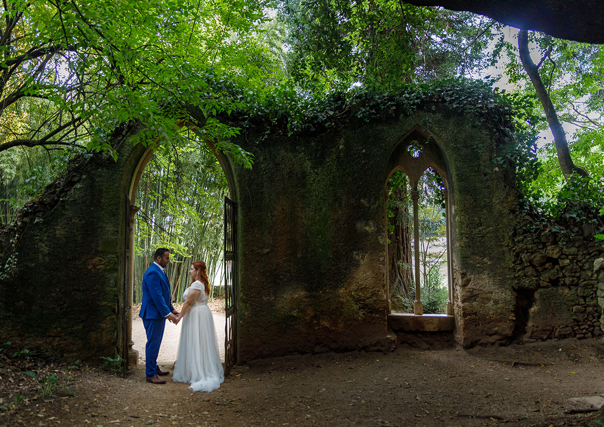 Enquadrados pela porta em arco da antiga parede coberta de trepadeiras, Mónica e Ricardo dão-se as mãos e olham-se em silêncio, num momento de pura conexão e reflexão. O verde da natureza e o musgo nas pedras envolvem-nos como um sussurro do tempo.
