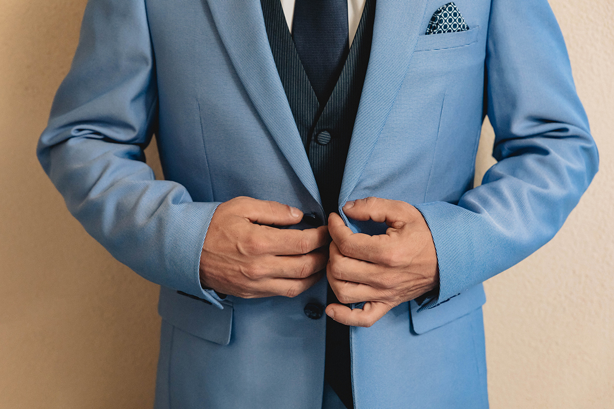 Com mãos seguras, afina os últimos detalhes, o colete, a gravata, o lenço com bolinhas, cada peça alinhada com o amor que irá selar.