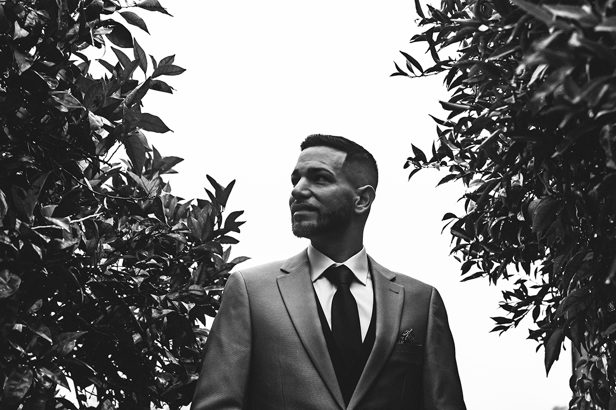 Num ângulo poético, o céu e as laranjeiras emolduram o noivo, que ergue a cabeça com esperança e serenidade.