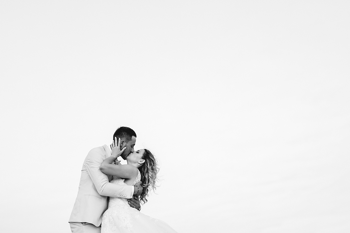 Foto a preto e branco, com fundo claro. À esquerda, os dois beijam-se intensamente, ele com a mão nas costas dela, e ela com as mãos na cabeça dele.