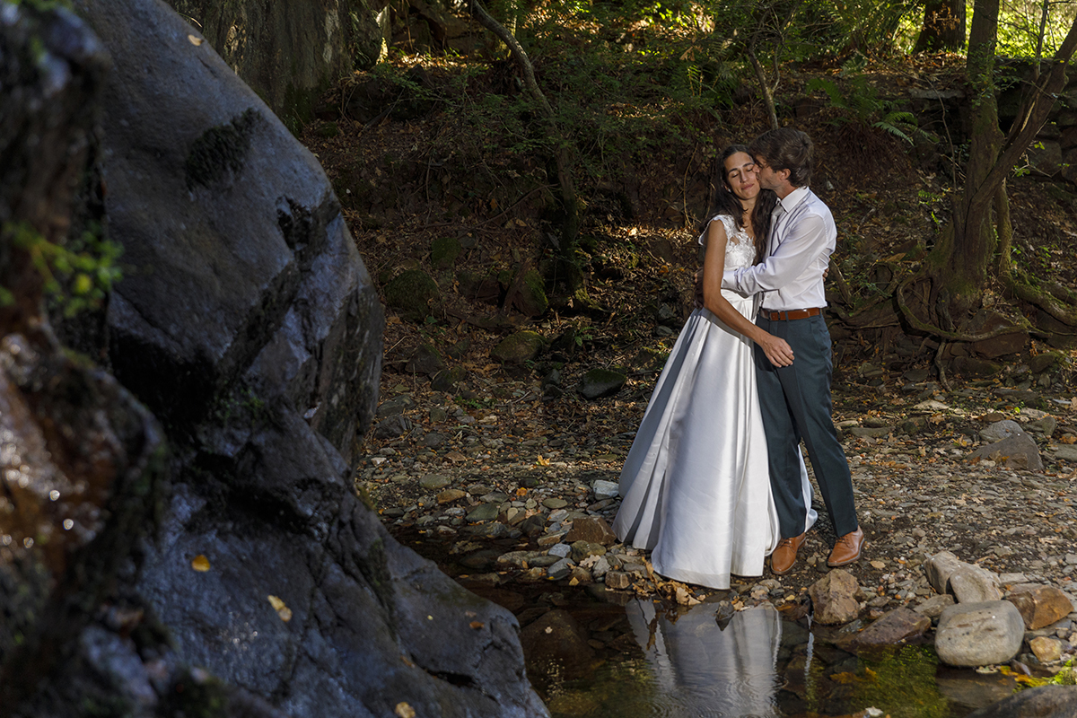 Num plano mais próximo, os dois abraçam-se suavemente. Ele beija-lhe a bochecha e ela sorri levemente. O cenário natural à volta parece abençoar o momento.