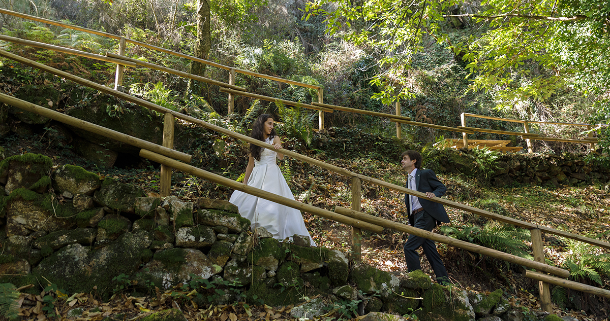 A subir uma rampa de pedra, Diana vai à frente, sorrindo para André. Ele retribui o olhar com alegria. As mãos no corrimão de madeira marcam o caminho do amor partilhado.