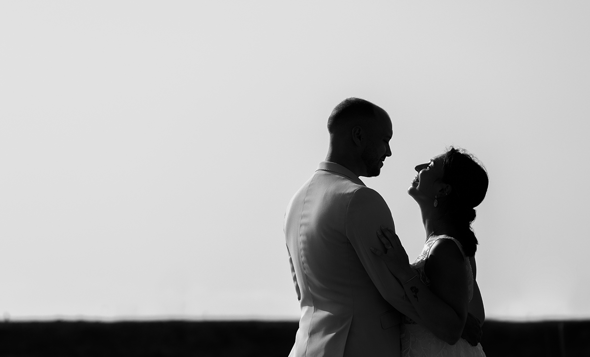 Foto com fundo branco e barra preta inferior. No canto direito, Patrícia e Bruno olham-se serenamente. Bruno tem a mão nas costas dela, enquanto Patrícia segura-lhe o braço.