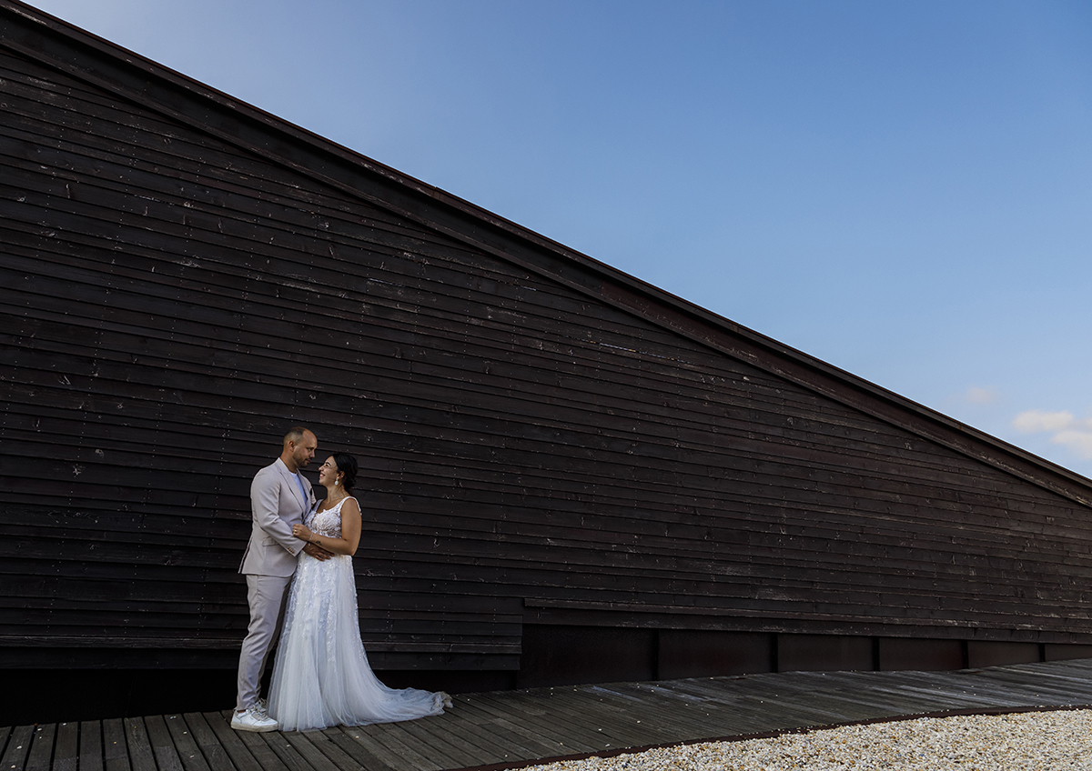 Os pombinhos estão encostados a uma bonita parede de madeira que desce suavemente. Estão virados um para o outro, Bruno coloca a mão na barriga de Patrícia e trocam olhares felizes.