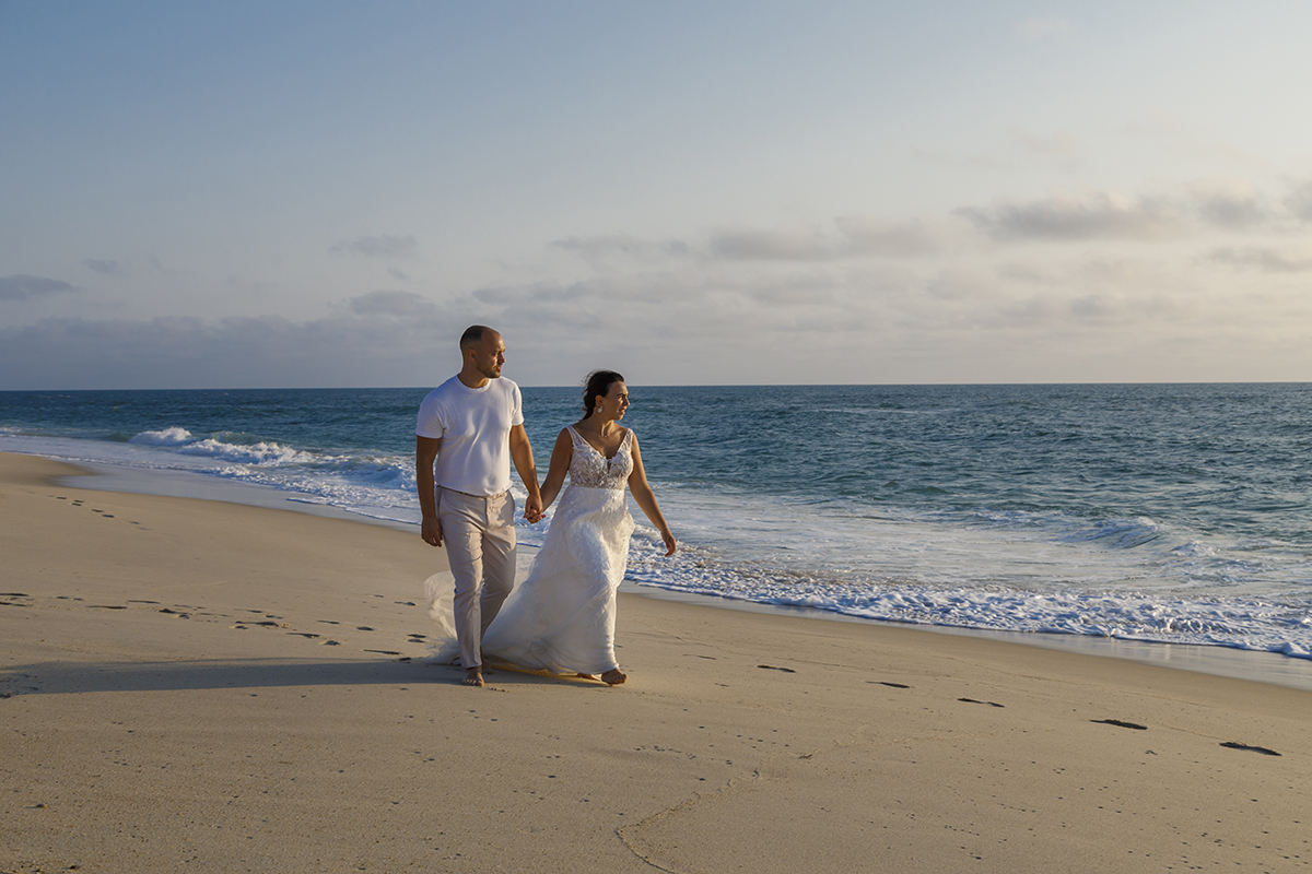 Junto ao mar, os dois caminham de mãos dadas, a olhar para o oceano. A luz do sol toca-lhes o corpo num momento calmo e feliz.