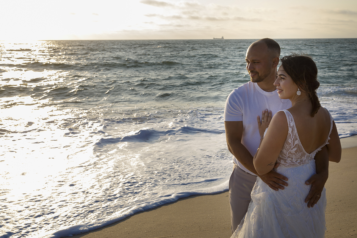 Num plano mais fechado, vê-se apenas um pouco de areia. No lado direito, Bruno segura Patrícia pela cintura, enquanto ela coloca as mãos no peito dele. Ambos sorriem e olham para o lado.