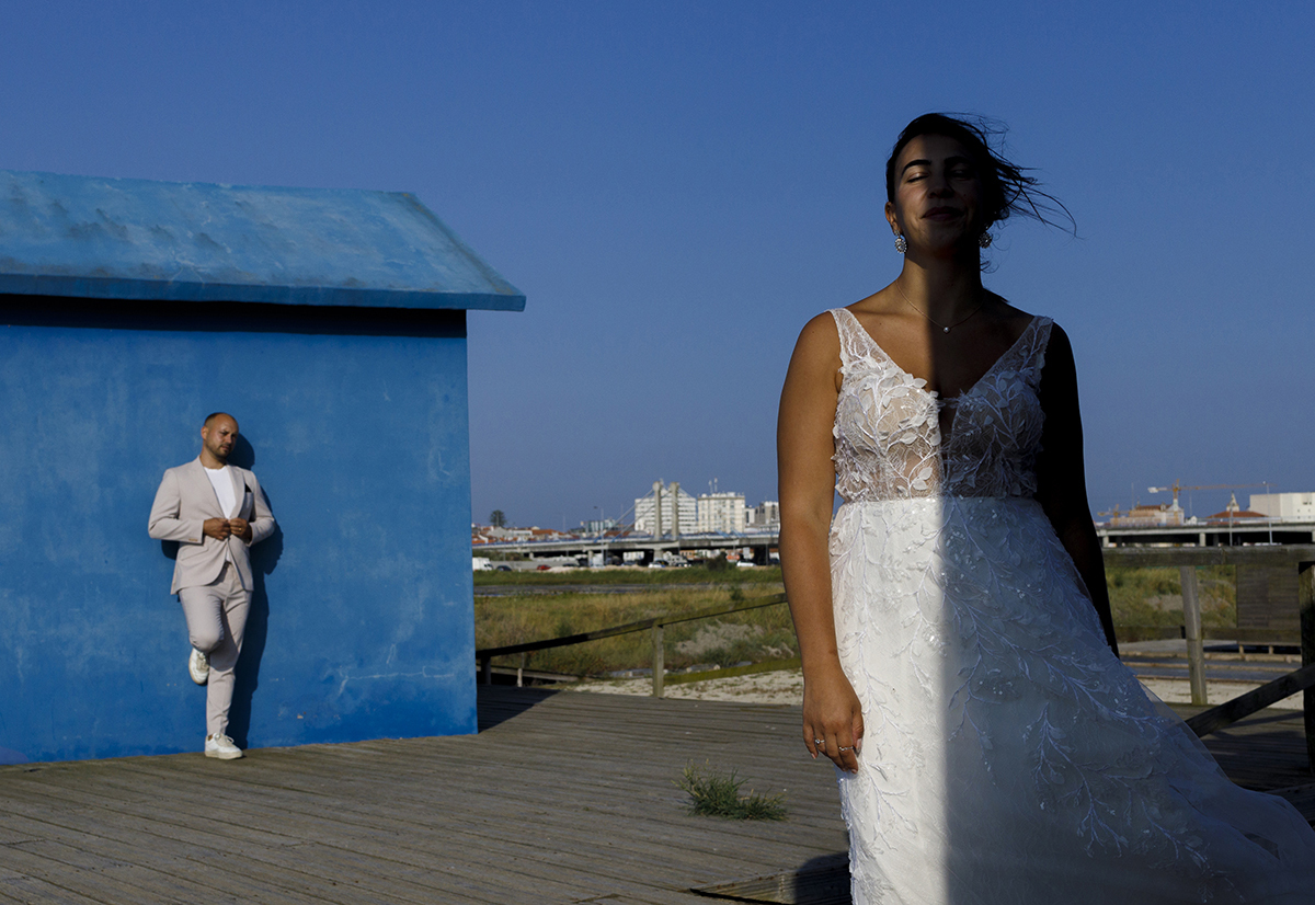 Agora é Patrícia quem está em destaque com o efeito de sol e sombra, enquanto Bruno está mais atrás, encostado a uma casinha azul, sereno e tranquilo.