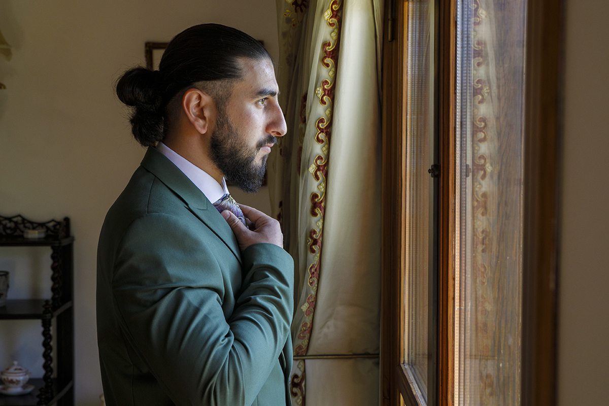 Furkan contempla a luz da janela, sério e pensativo, com a mão na gravata.