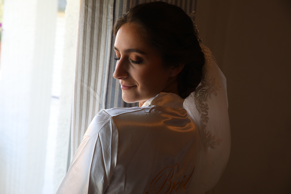 Carolina, iluminada pela luz da janela, olha em direção à lente, refletindo serenidade e felicidade.